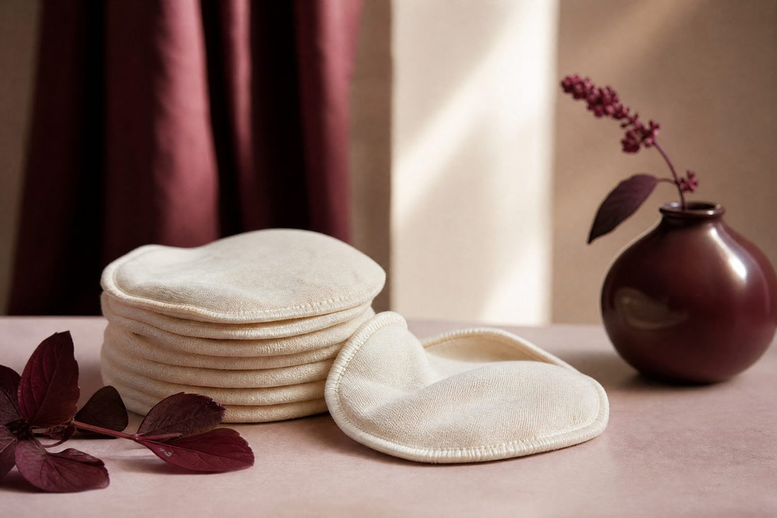 Coussinets d'allaitement en coton creme plies sur une surface pastel