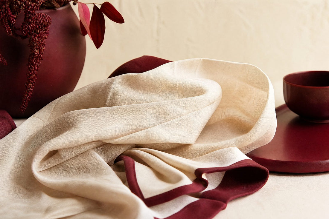 Tissu de coton creme respirant plie doucement avec une bordure bordeaux